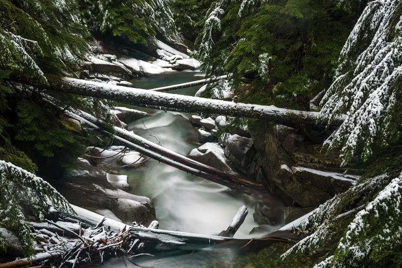 long-exposure-of-a-river-with-snow-on-logs-in-the