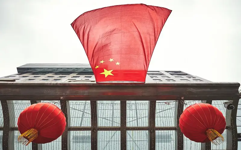 Looking up at Chinese flag and red lanterns on a building.