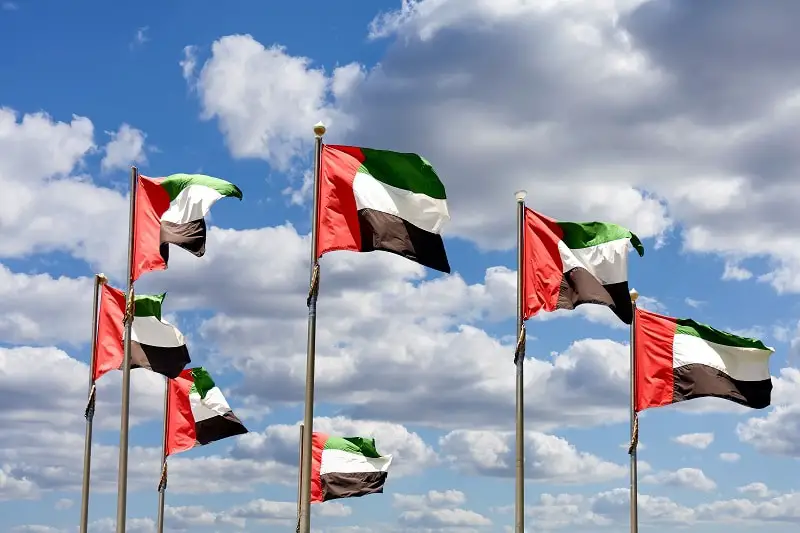 Seven United Arab Emirates flags against blue sky with clouds.