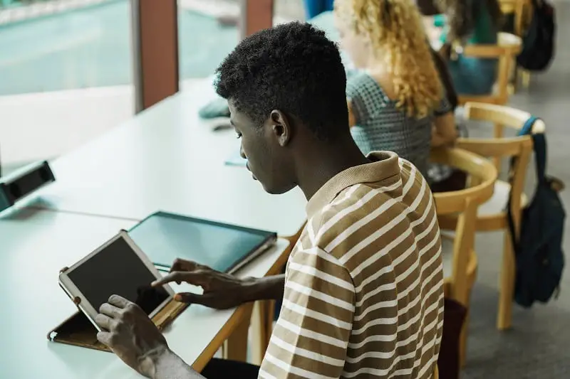 Young multiethnic group of students studying inside university library - Main focus on african guy ear