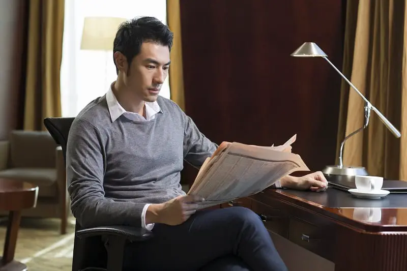 Young Chinese businessman reading newspaper in study
