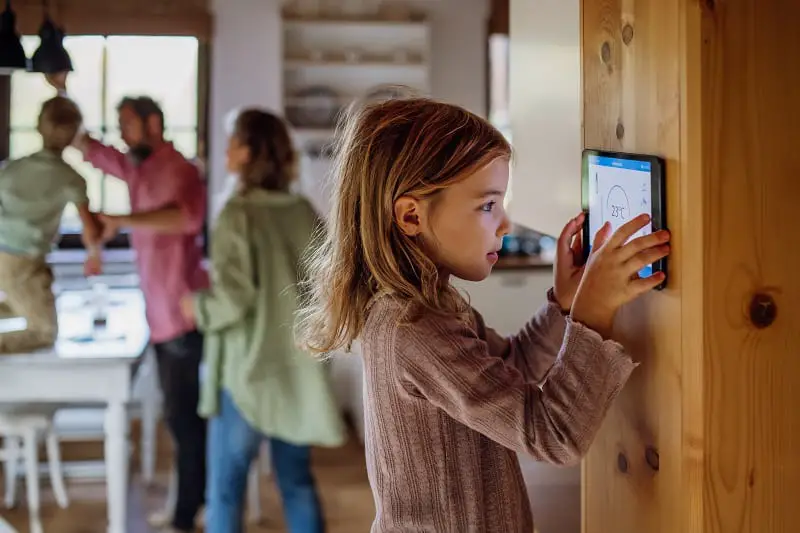 Girl looking at smart thermostat at home, checking heating temperature. Concept of sustainable, efficient, and smart technology in home heating and thermostats.