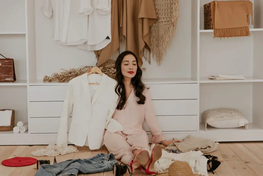 Brunette pretty woman in pink pajamas and high heels sits on floor in white dressing room surrounde